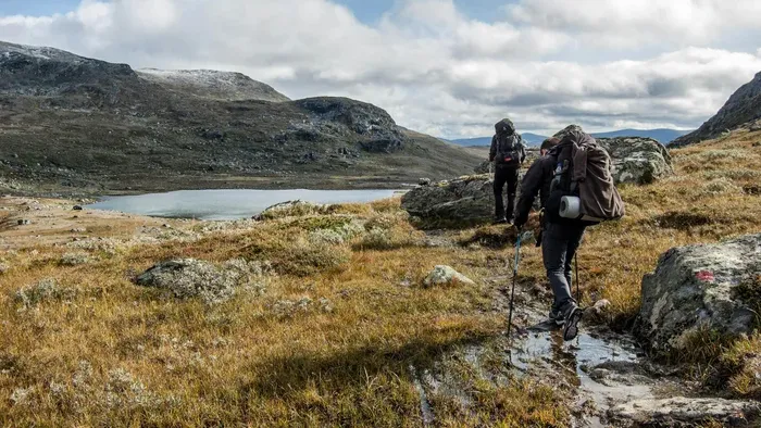 Two hikers with backpacks walking a trail across open moorland beside a mountain lake