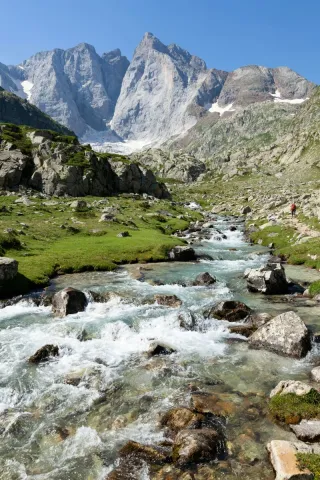 Mountain stream flowing through a green alpine valley with views of the rocky faces of Vignemale under a clear sky.